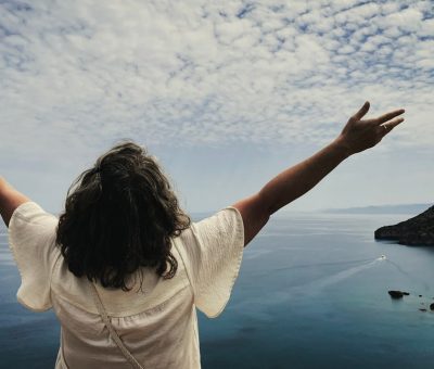 Woman with arms outstretched overlooking the ocean.